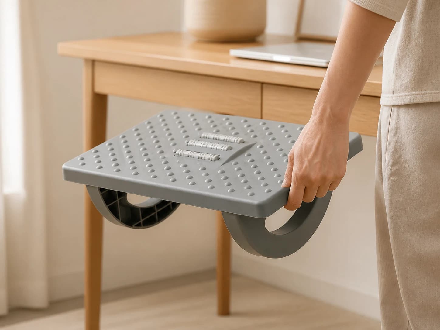 Person lifting the compact RollArc footrest beside a desk