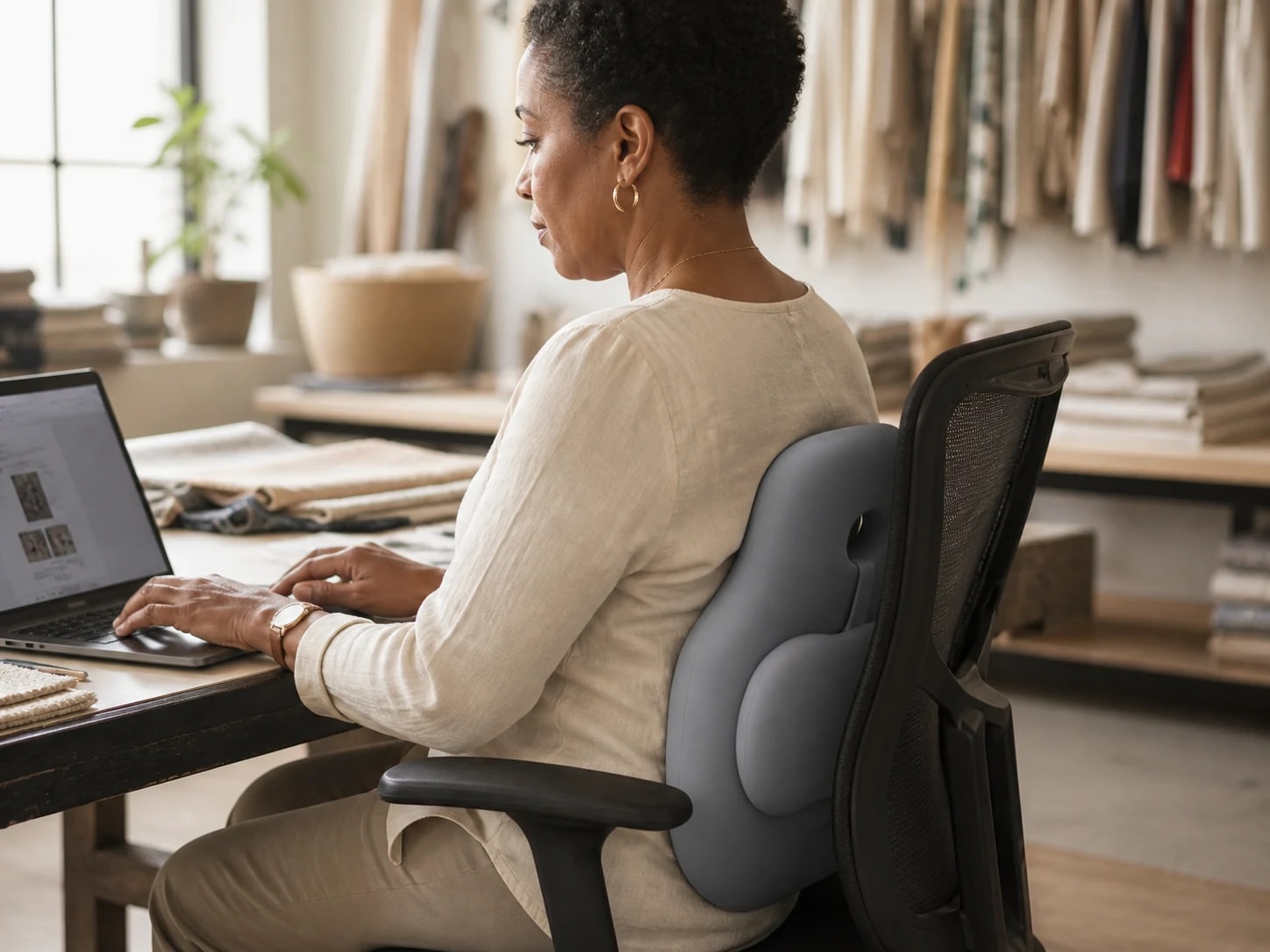 Seated adult using the volcanic-gray HaloBack cushion at a textile-studio worktable