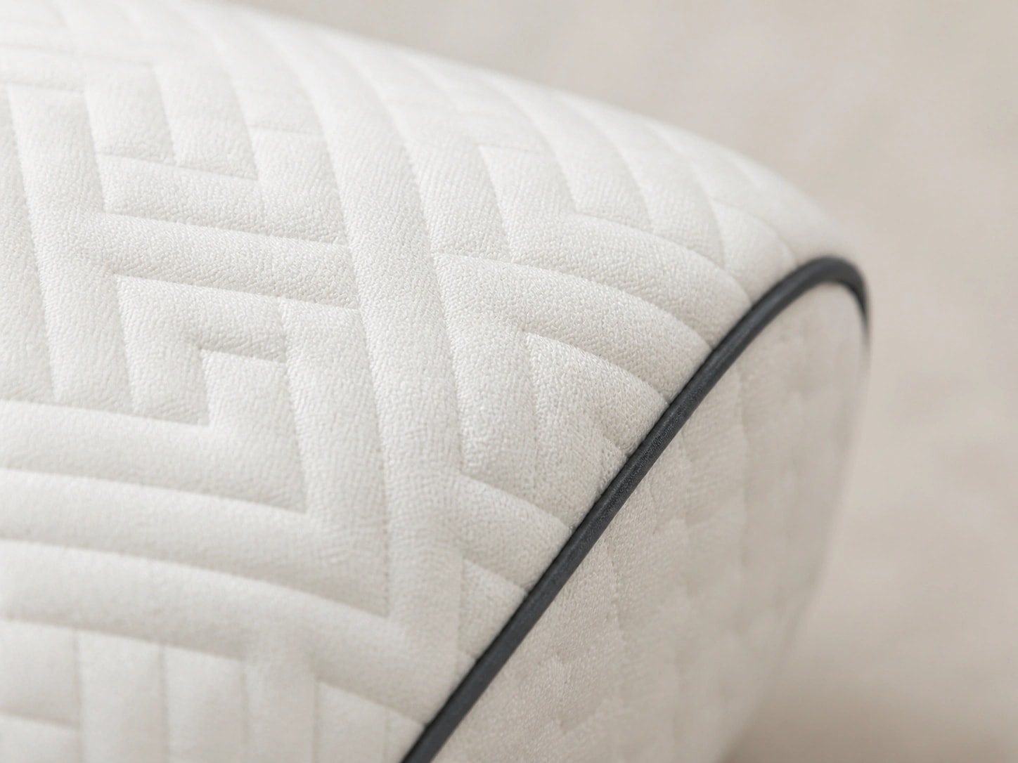 Macro view of WaveRest's white maze-pattern fabric, thin dark piping, underside zipper, and inner sleeve